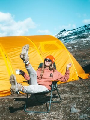 Happy female sitting on chair near tent on mountain slope